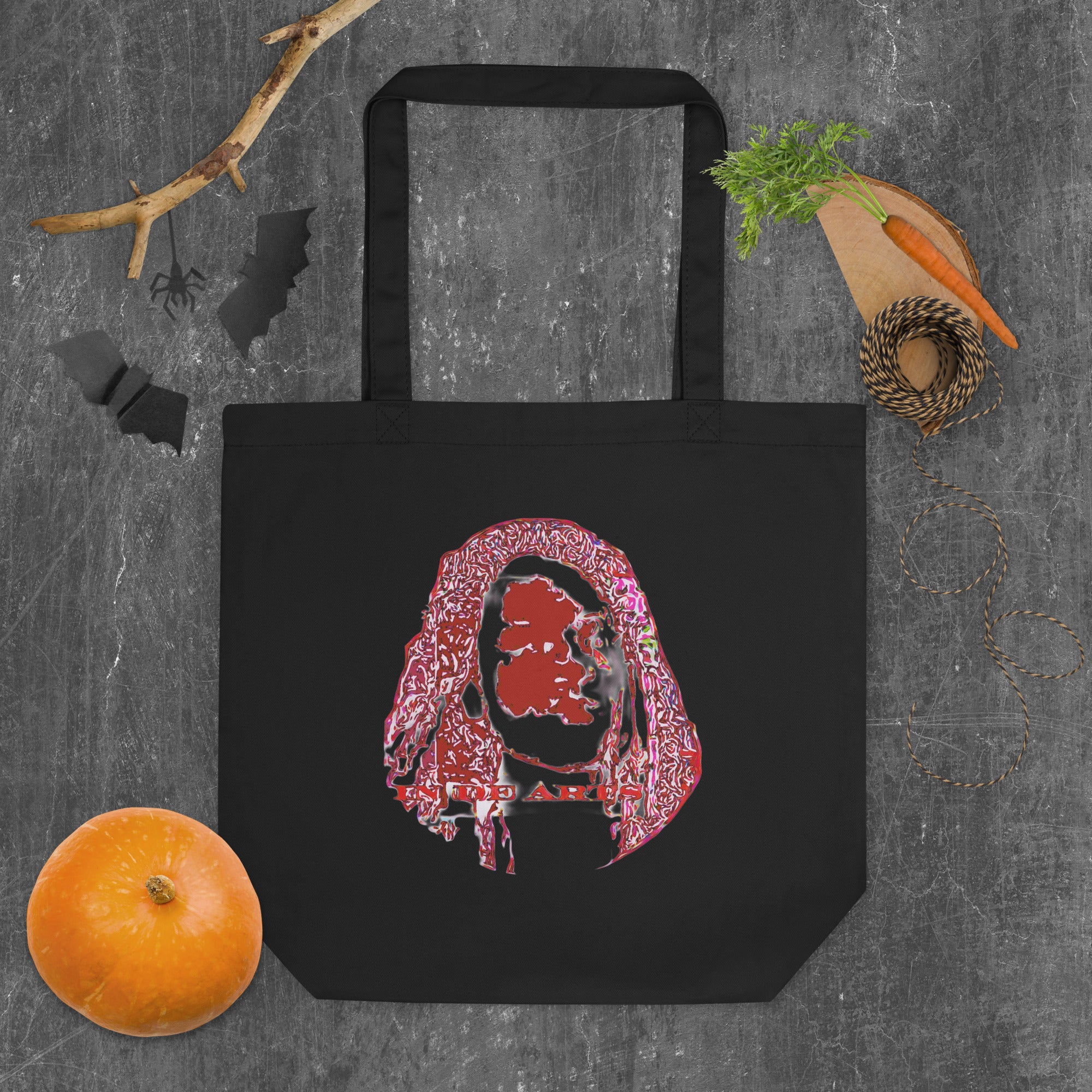 Black tote bag with a colorful graphic design on a textured gray surface with vegetables.
