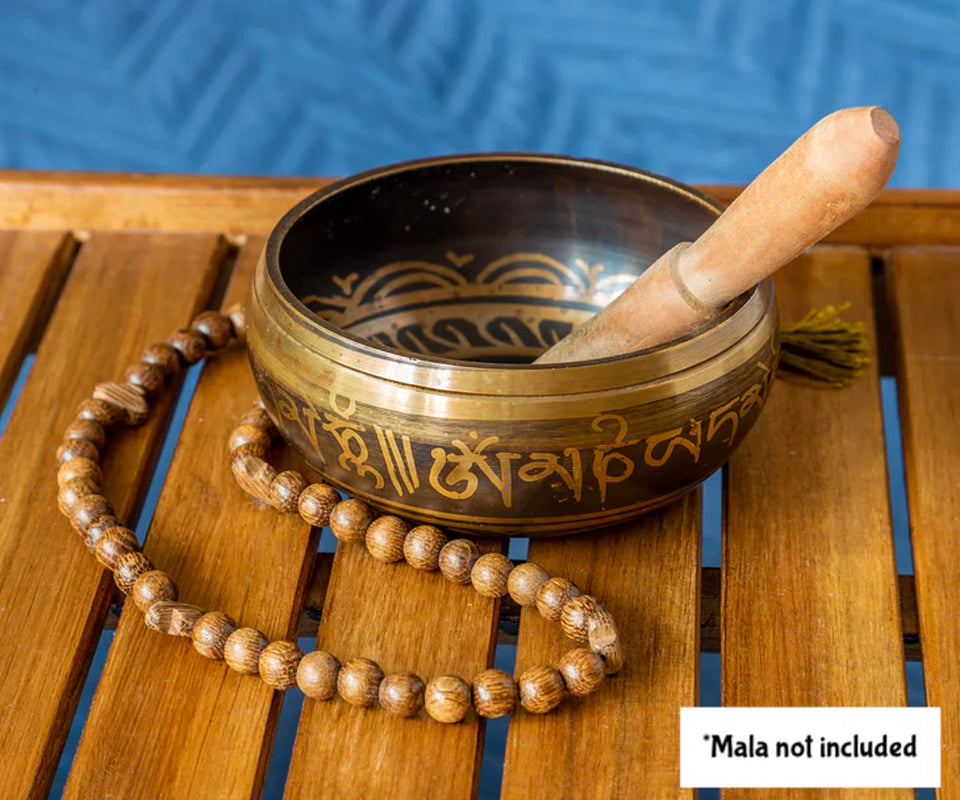 Tibetan singing bowl with wooden beater and mala on a wooden surface with blue background